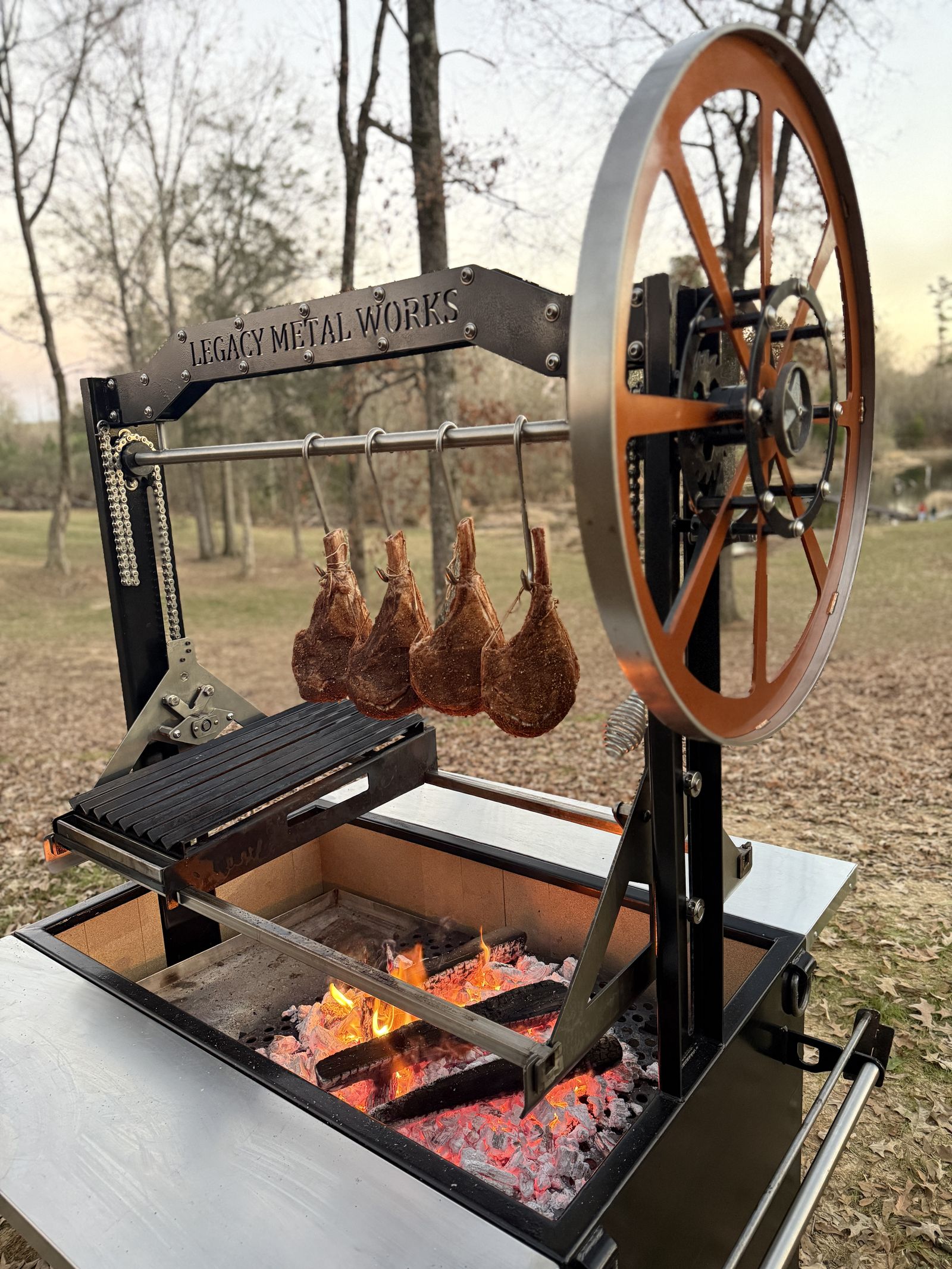 Legacy Metal Works gaucho grill with hanging tomahawks at dusk